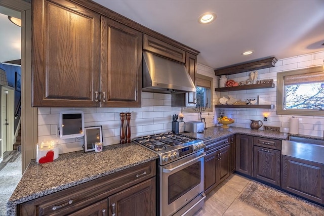 kitchen featuring high end stainless steel range, dark stone counters, decorative backsplash, ventilation hood, and dark brown cabinets