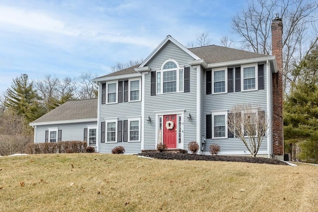 colonial home with a chimney, a front yard, and a shingled roof