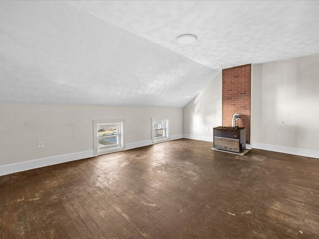 additional living space with a textured ceiling, vaulted ceiling, a wood stove, and dark hardwood / wood-style flooring