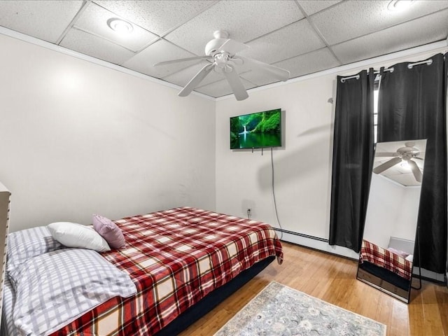 bedroom with hardwood / wood-style floors, crown molding, a baseboard heating unit, ceiling fan, and a paneled ceiling