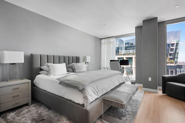 bedroom with expansive windows, baseboards, multiple windows, and wood finished floors