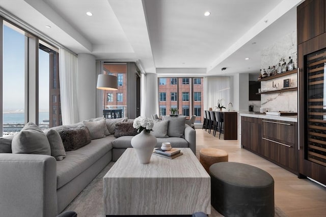 living area with recessed lighting, a raised ceiling, bar, and light wood finished floors