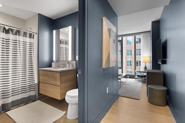 bathroom with vanity, wood finished floors, toilet, baseboards, and a shower with curtain