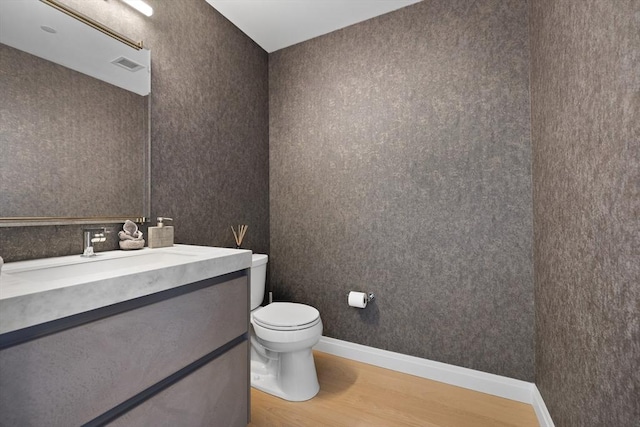 half bath featuring vanity, toilet, baseboards, wood finished floors, and visible vents