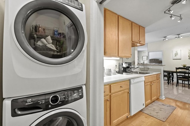 clothes washing area featuring sink, track lighting, stacked washer and clothes dryer, and light wood-type flooring