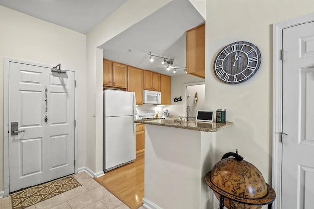 kitchen with white appliances, kitchen peninsula, dark stone counters, and light hardwood / wood-style flooring