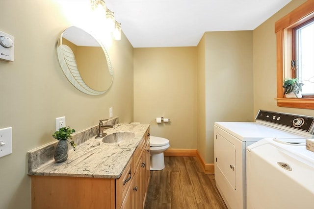 bathroom featuring washing machine and dryer, toilet, wood finished floors, vanity, and baseboards