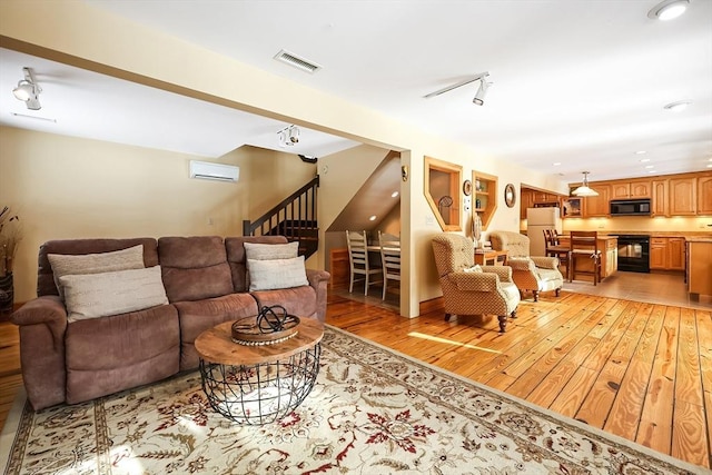 living room featuring visible vents, stairway, rail lighting, an AC wall unit, and light wood-style floors