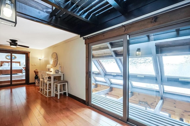 doorway to outside featuring hardwood / wood-style floors, a skylight, a ceiling fan, and baseboards