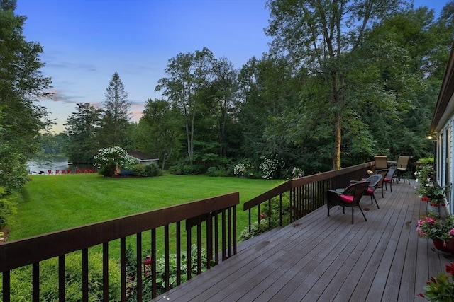 deck at dusk featuring a water view and a lawn