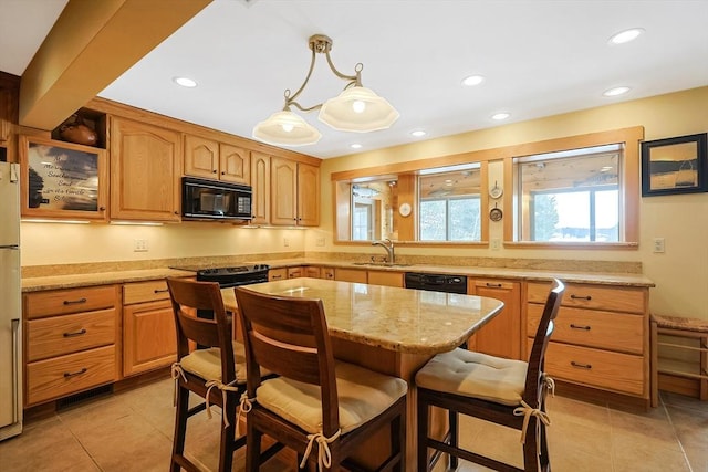 kitchen featuring a kitchen island, light stone counters, hanging light fixtures, black appliances, and a sink