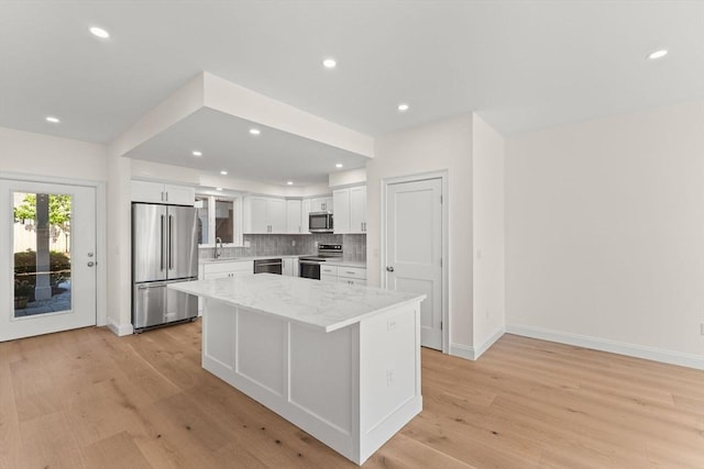 kitchen with stainless steel appliances, white cabinets, light wood-type flooring, a center island, and baseboards