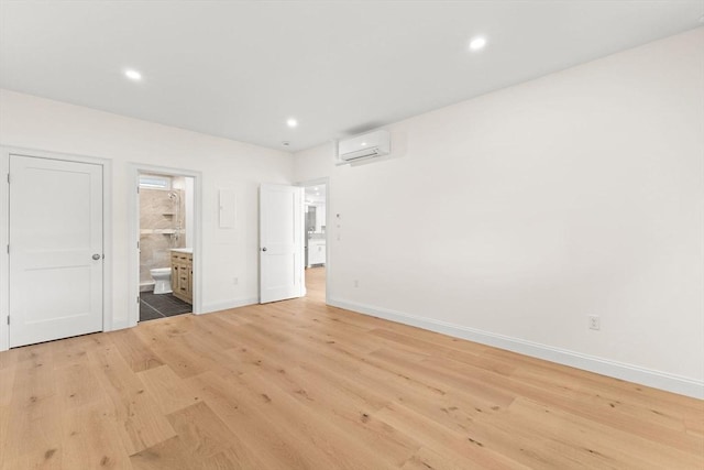unfurnished bedroom with a wall unit AC, baseboards, light wood-style floors, ensuite bath, and recessed lighting