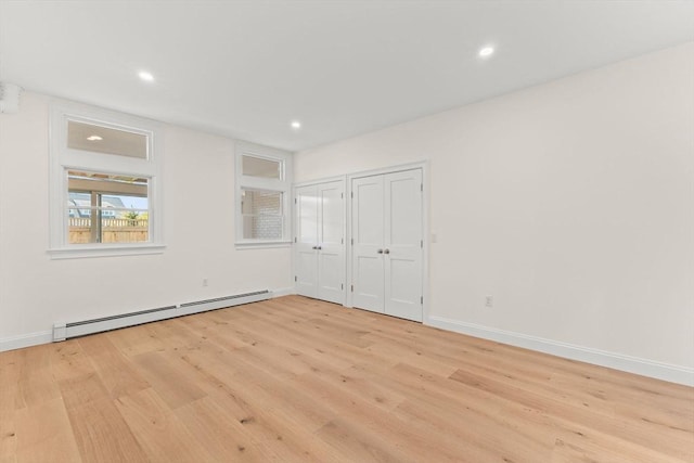 unfurnished bedroom with a baseboard heating unit, two closets, light wood-type flooring, recessed lighting, and baseboards