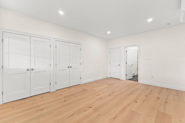 unfurnished bedroom with two closets, light wood finished floors, baseboards, and recessed lighting
