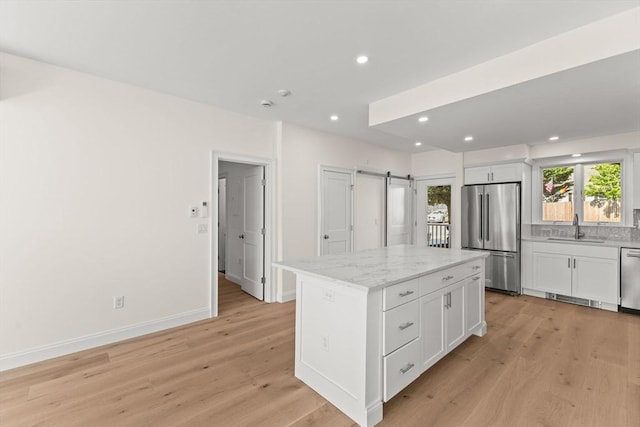 kitchen featuring stainless steel appliances, a sink, a barn door, white cabinetry, and light wood-type flooring