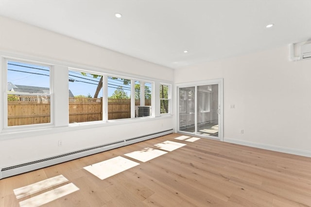 empty room featuring a baseboard radiator, wood finished floors, recessed lighting, baseboards, and a wall unit AC