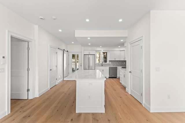 kitchen featuring stainless steel appliances, a barn door, white cabinets, a center island, and light wood-style floors