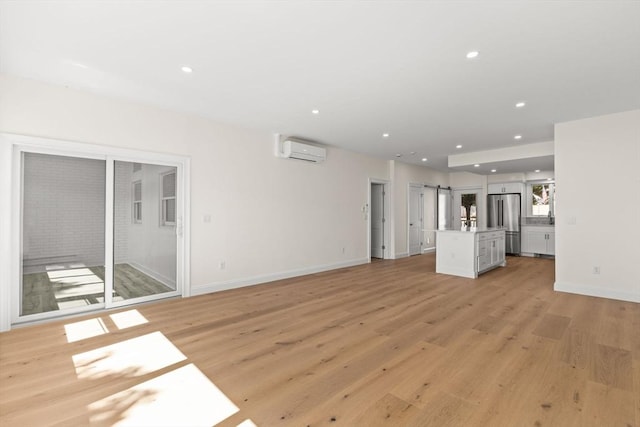 unfurnished living room featuring a barn door, light wood finished floors, a wall mounted AC, baseboards, and recessed lighting