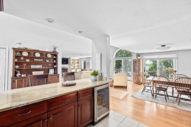 kitchen featuring beverage cooler, reddish brown cabinets, light stone counters, and a fireplace