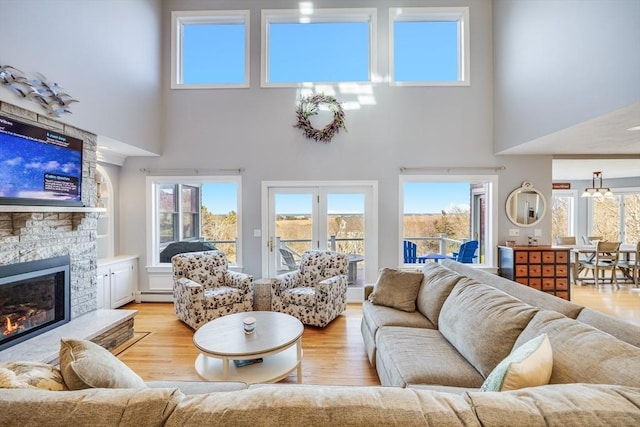 living area featuring a stone fireplace, light wood finished floors, and a baseboard radiator