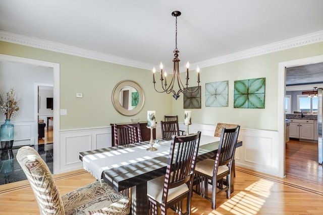 dining space featuring light wood finished floors, a wainscoted wall, crown molding, and an inviting chandelier