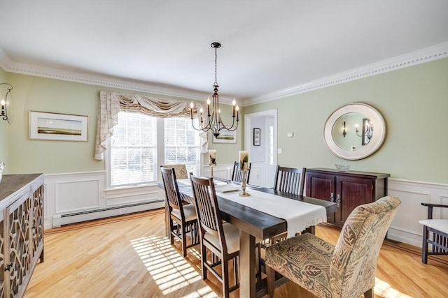 dining space with a chandelier, a wainscoted wall, ornamental molding, baseboard heating, and light wood-style floors