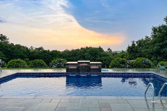 pool at dusk with a patio and an outdoor pool