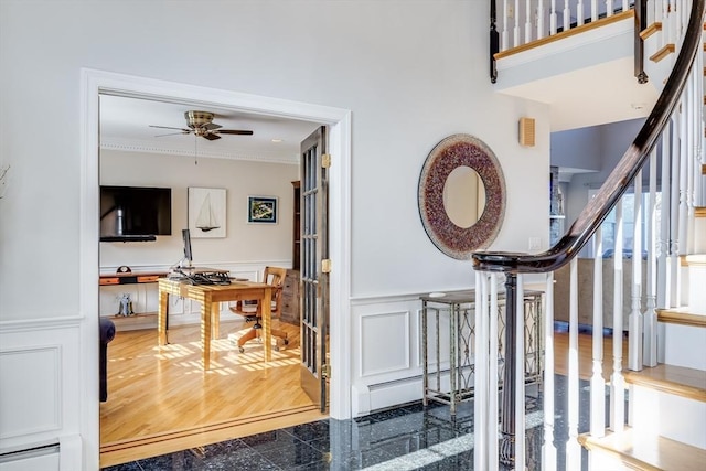 foyer entrance with crown molding, a baseboard heating unit, a wainscoted wall, granite finish floor, and a ceiling fan