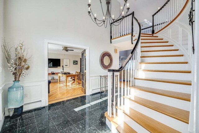 entryway featuring a wainscoted wall, a baseboard heating unit, granite finish floor, a decorative wall, and a towering ceiling