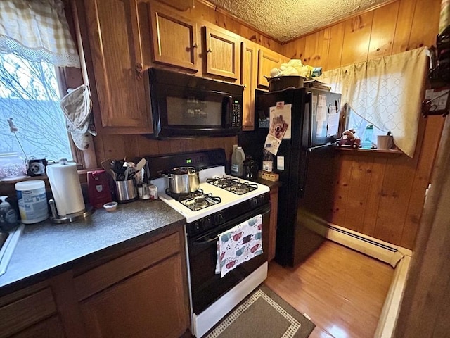 kitchen featuring wood walls, black appliances, and a baseboard heating unit