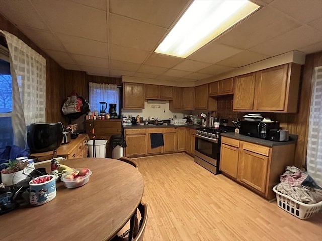 kitchen featuring stainless steel gas stove, a drop ceiling, light wood-type flooring, and sink