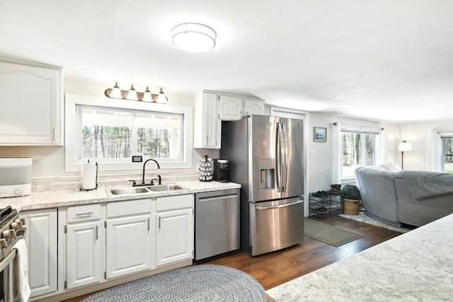 kitchen with dark wood finished floors, a sink, open floor plan, stainless steel appliances, and white cabinetry