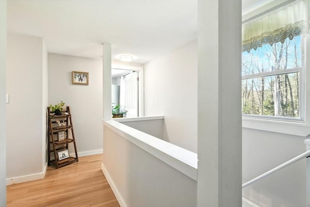 corridor featuring baseboards, light wood-style flooring, and an upstairs landing