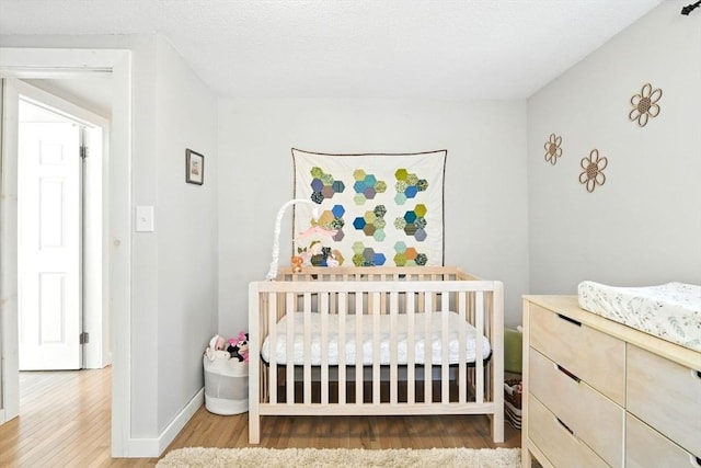 bedroom featuring a nursery area, baseboards, and wood finished floors