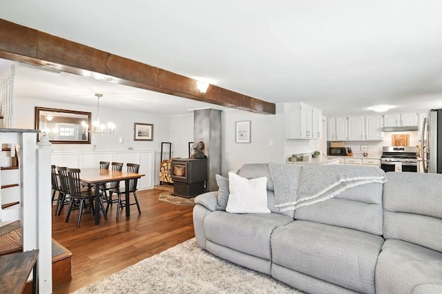 living room featuring beam ceiling, a chandelier, wood finished floors, and a wood stove