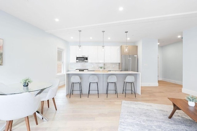 kitchen featuring stainless steel appliances, a kitchen island with sink, decorative light fixtures, light hardwood / wood-style flooring, and white cabinets