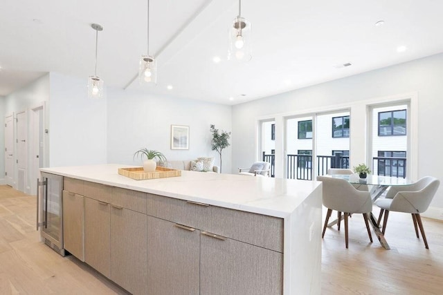 kitchen featuring light brown cabinets, beverage cooler, hanging light fixtures, a kitchen island, and light wood-type flooring