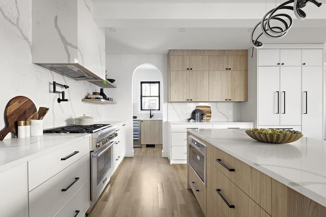 kitchen featuring island range hood, stainless steel range, beverage cooler, light stone countertops, and white cabinets