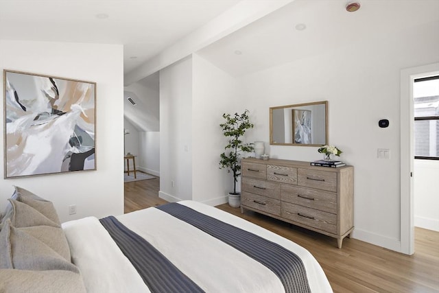 bedroom with lofted ceiling with beams and light hardwood / wood-style floors