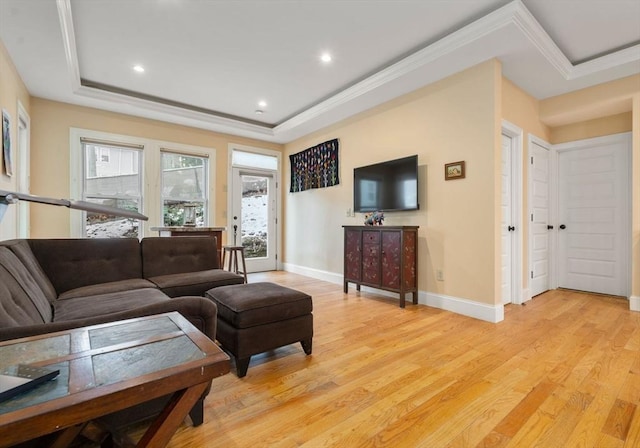 living room featuring crown molding, light wood-type flooring, and a tray ceiling