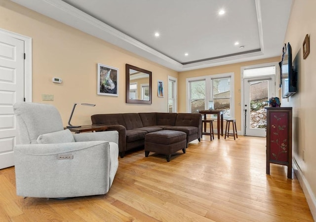 living room with ornamental molding, a tray ceiling, and light wood-type flooring