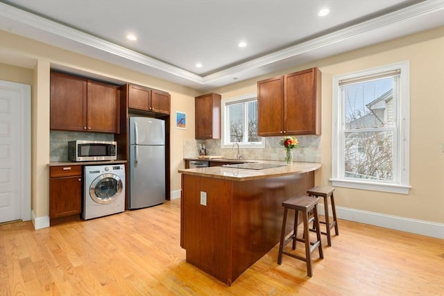 kitchen featuring appliances with stainless steel finishes, a kitchen breakfast bar, a raised ceiling, washer / dryer, and kitchen peninsula