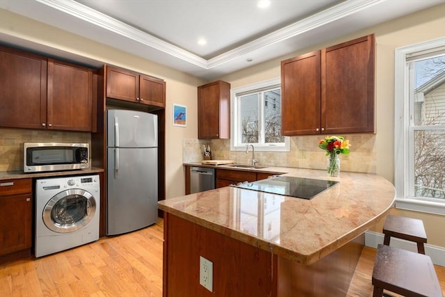 kitchen featuring washer / clothes dryer, a breakfast bar area, kitchen peninsula, stainless steel appliances, and light stone countertops