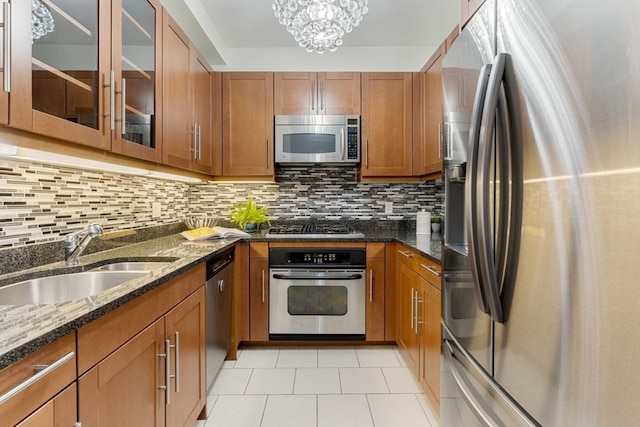 kitchen with stainless steel appliances, decorative backsplash, sink, dark stone countertops, and light tile patterned floors