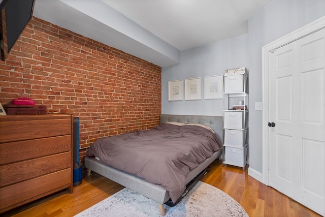 bedroom featuring brick wall and light wood-type flooring