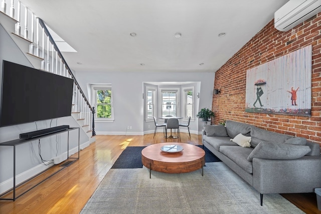 living room with lofted ceiling, a wall mounted AC, brick wall, and light hardwood / wood-style flooring