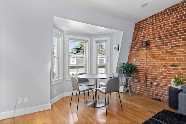 dining area with brick wall and light hardwood / wood-style floors