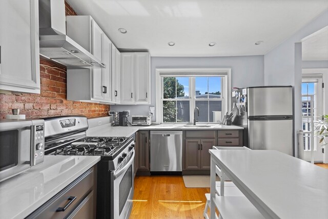 kitchen with white cabinets, appliances with stainless steel finishes, light hardwood / wood-style floors, sink, and wall chimney exhaust hood