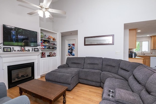 living room featuring a ceiling fan, high vaulted ceiling, a glass covered fireplace, and light wood finished floors